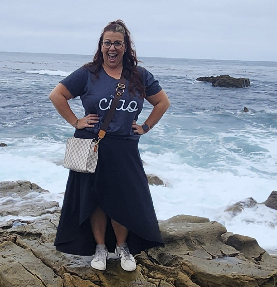 Victoria Mallon standing next to the sea on a cliffside in a dress and a tshirt